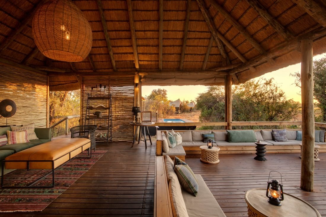 The open-sided lounge at Camp Khwai under its thatched roof, looking out towards the pool in golden afternoon light.