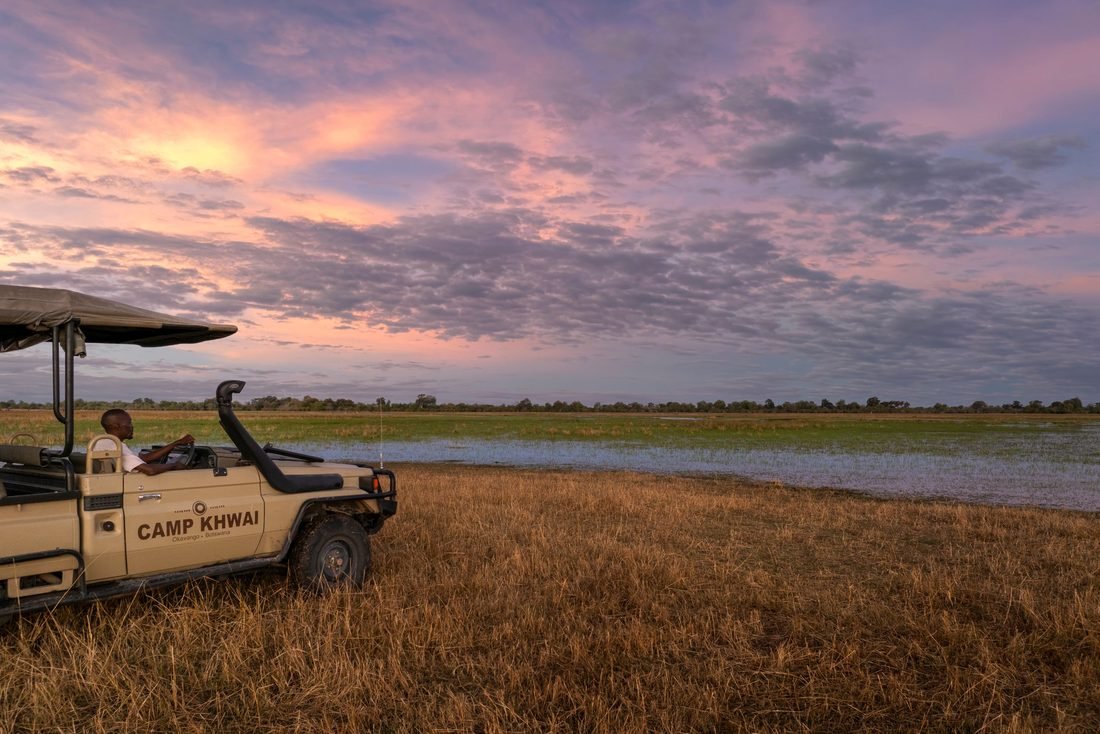 A Camp Khwai game viewer parked at the edge of a flooded Khwai floodplain under a pink evening sky.