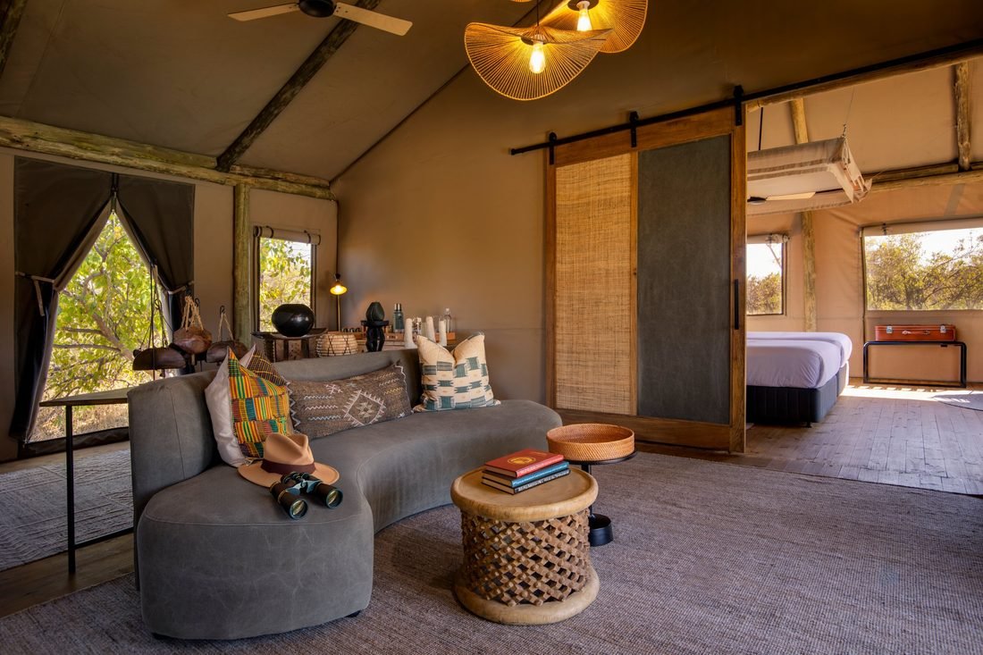 The lounge area of a Camp Khwai tented suite, with a curved sofa, binoculars and a hat on the cushions.